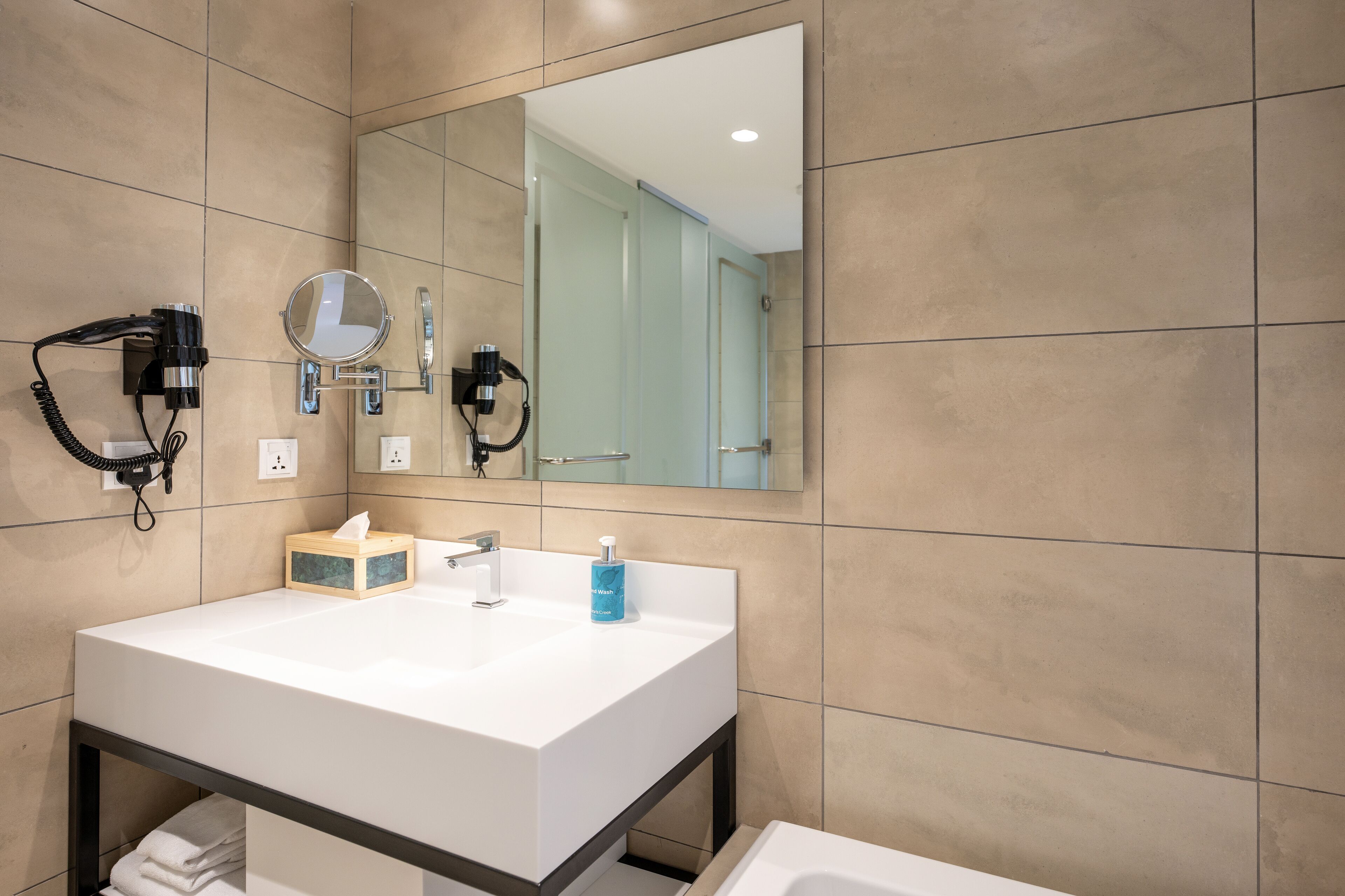 Un baño moderno con un lavamanos blanco, un espejo grande y un secador de pelo montado en la pared.