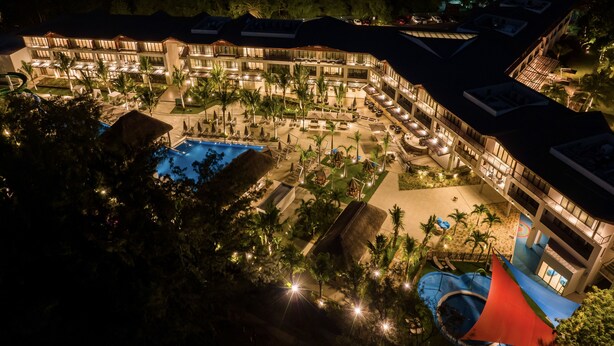 Un complexe hôtelier doté de plusieurs piscines, de palmiers et d’un bâtiment bien éclairé.