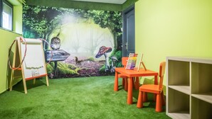 A room with a green carpet, a whiteboard, a table with chairs, and a mural of a forest scene.