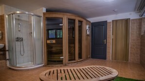 A bathroom with a glass-enclosed shower, a wooden door, and a small table with a green rug.