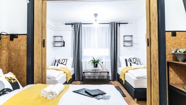 A hotel room with two beds, a small table with a plant, and a view of the city through large windows.