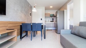 Een moderne woonkamer met een bank, een eettafel met stoelen, een aan de muur bevestigde televisie en een keuken in de achtergrond.