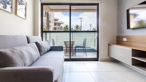 Een moderne woonkamer met een grijze bank, een aan de muur bevestigde televisie en een balkon met een stoel.