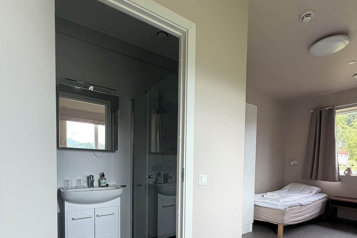A bedroom with a bed, a window with curtains, and a bathroom with a sink and mirror.