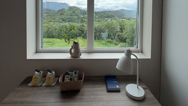 A room with a large window, a desk with a lamp, a vase, and a basket.