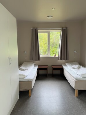 Une chambre avec deux lits simples, une fenêtre avec des rideaux, un bureau et une armoire.