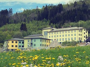 Ein mehrstöckiges Gebäude mit einer gelb-grünen Fassade, umgeben von einem Feld gelber Blumen.