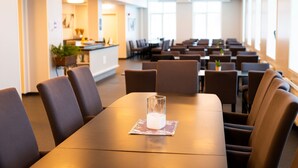 A conference room with a long table, multiple chairs, and a glass of water on a coaster.