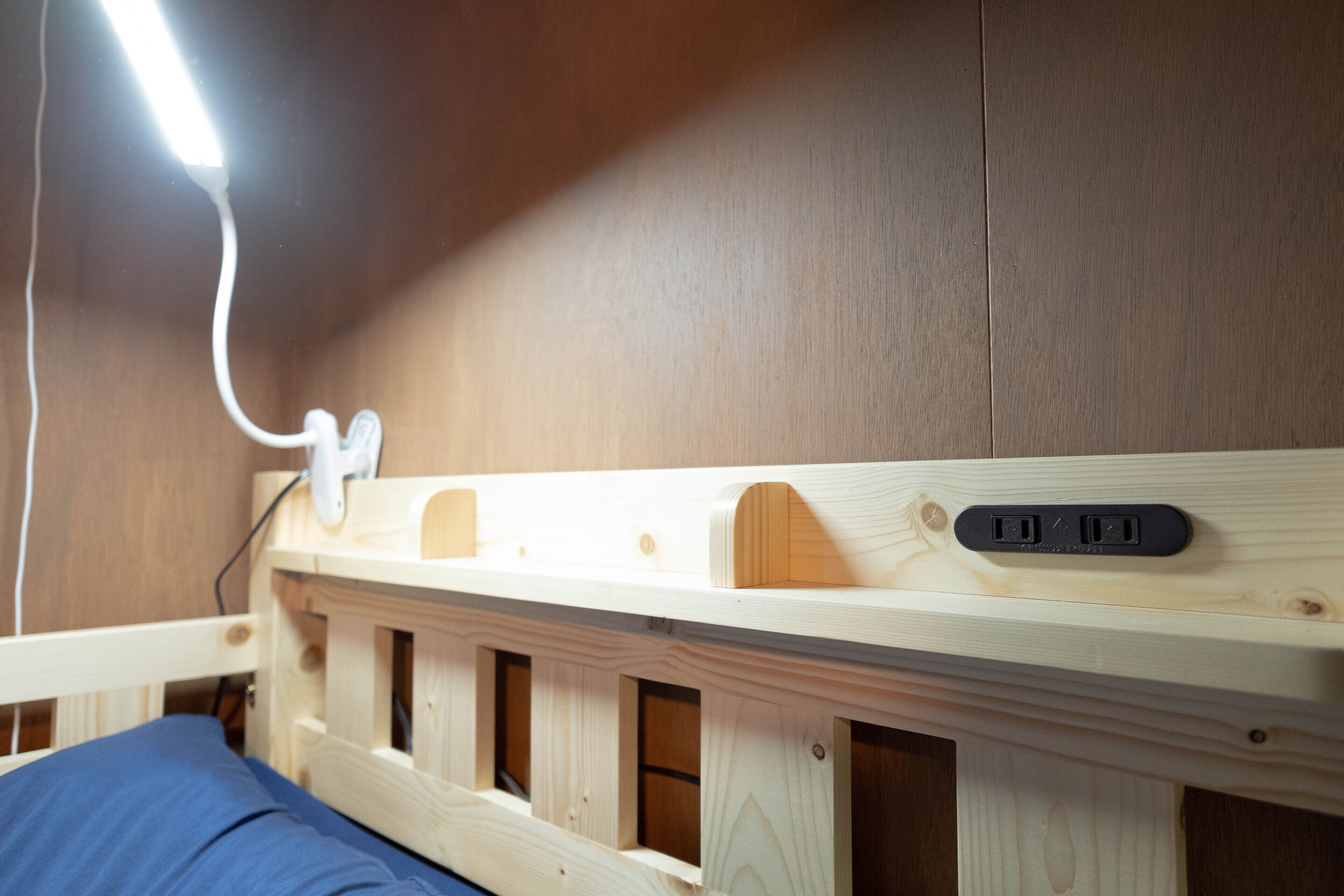 A wooden bunk bed with a headboard that includes a power outlet and USB ports.