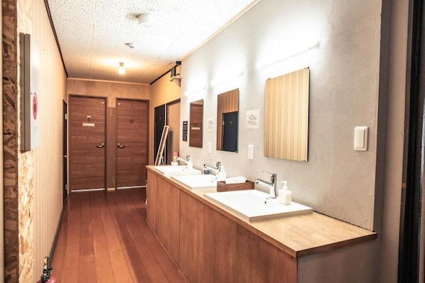 A modern bathroom with wooden flooring, a long vanity with three sinks, and wooden doors. - Little Japan Echigo (Yuzawa)