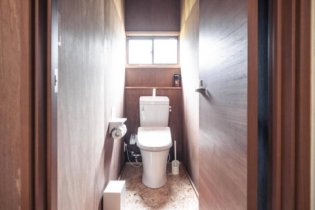 Un baño pequeño y estrecho con inodoro, una ventana y un estante de madera.