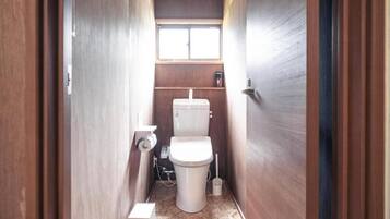 Un baño pequeño y estrecho con inodoro, una ventana y un estante de madera.