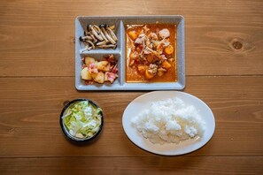 A meal with rice, a salad, and a dish containing meat and vegetables on a wooden table. - Little Japan Echigo (Yuzawa)