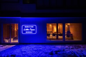 A building with a neon sign reading "Ryokaku & Cafe Little Japan ECHIGO" and large glass doors leading to an interior with tables and chairs. - Little Japan Echigo (Yuzawa)
