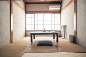 Una habitación con esteras de tatami, una mesa baja, un cojín y una ventana con vistas.