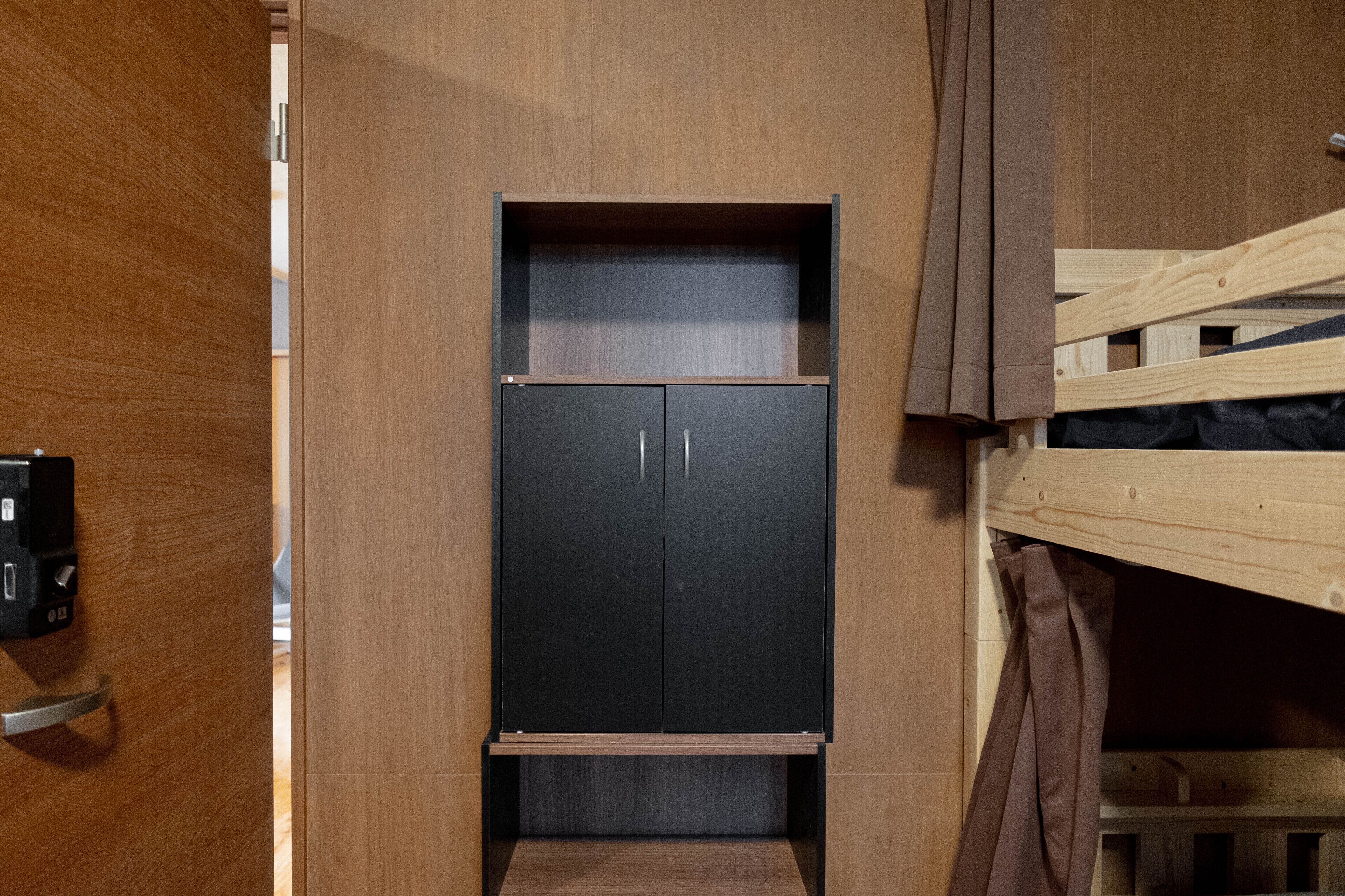 A compact room with a wooden wardrobe, a small desk, and a bunk bed.