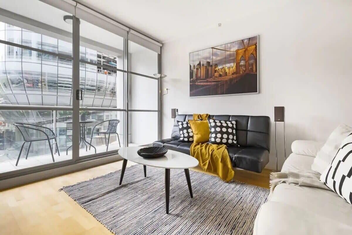 A modern living room with a sofa, a coffee table, and a large window with a city view.