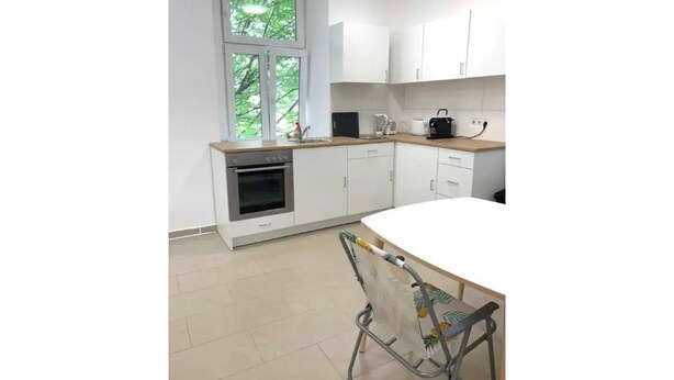 Une cuisine moderne avec des meubles blancs, un four encastré et une fenêtre donnant sur un paysage verdoyant.