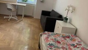 Une pièce comprenant un lit, un bureau, une chaise, une fenêtre avec des rideaux et une plante en pot.