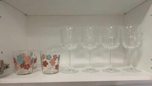 Une étagère avec quatre verres à vin transparents et deux récipients en verre ornés de motifs floraux.