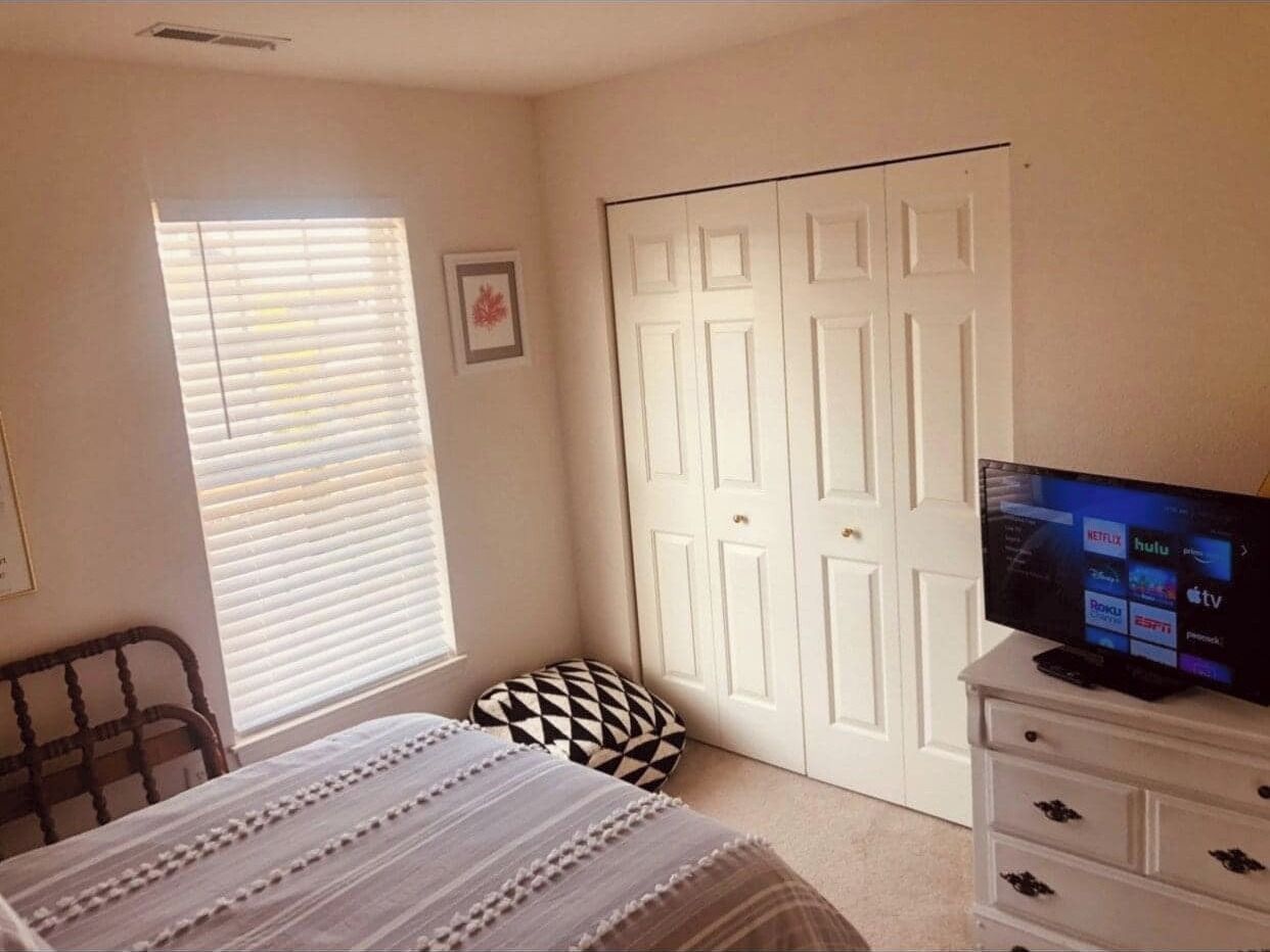 A bedroom with a bed, a TV, a dresser, a window with blinds, and a closet.