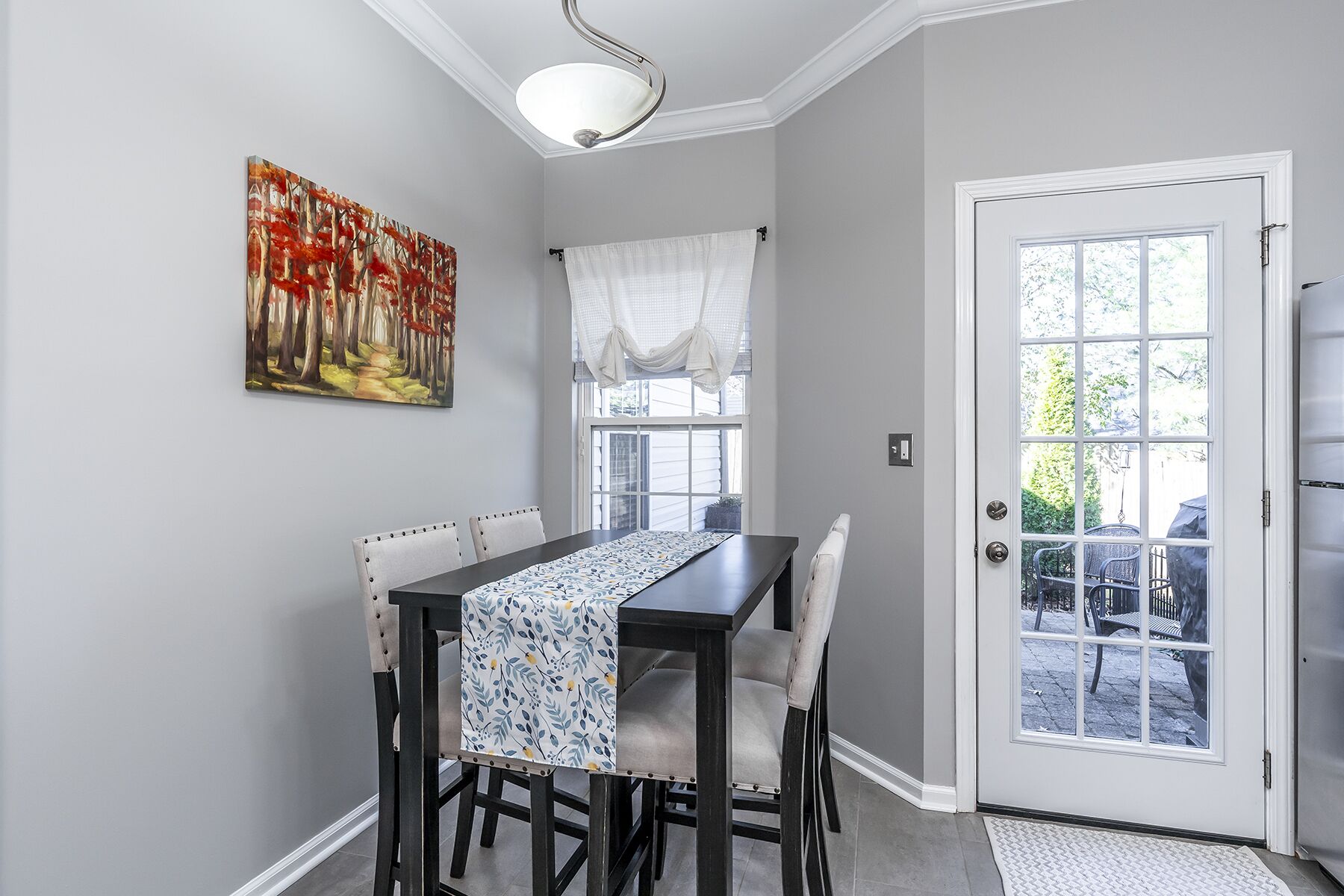 Un coin repas avec une table dressée pour quatre personnes, un tableau accroché au mur et une porte donnant sur l’extérieur.