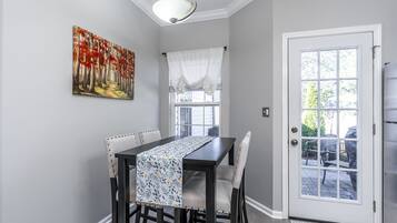 Un coin repas avec une table dressée pour quatre personnes, un tableau accroché au mur et une porte donnant sur l’extérieur.