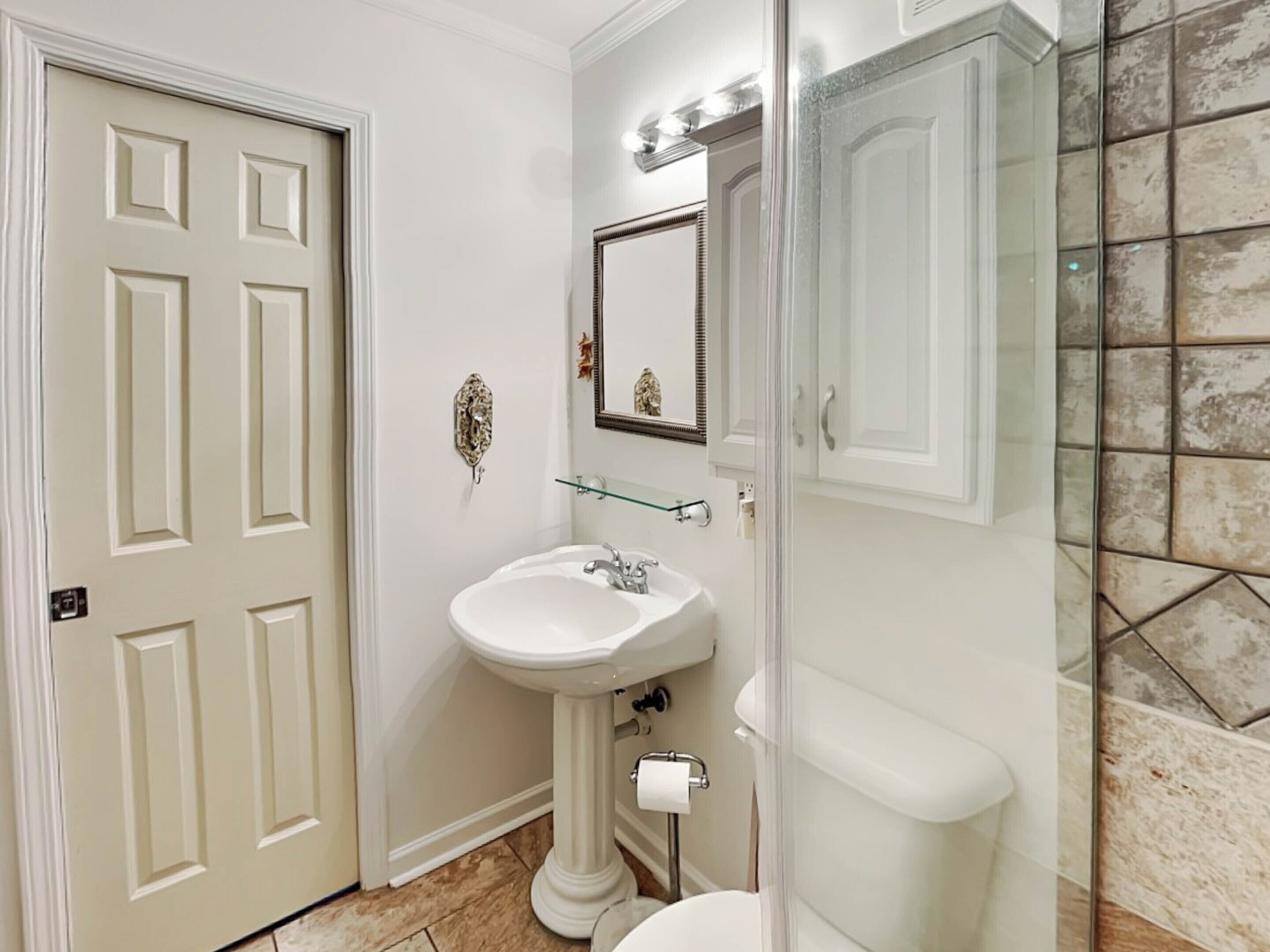 Une salle de bain avec un lavabo sur colonne, des toilettes et une douche à parois de verre.