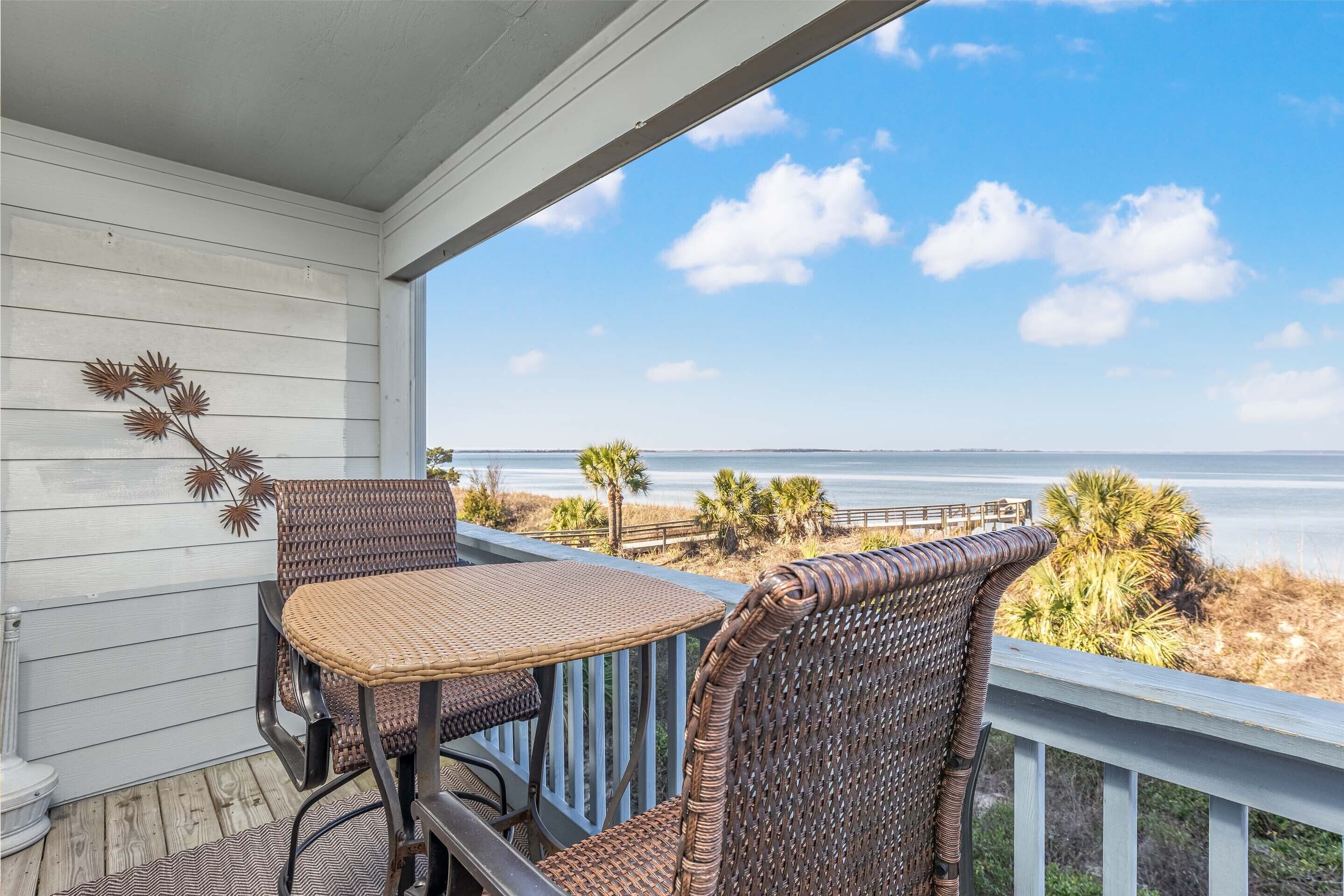 A balcony with wicker furniture overlooking a beach.