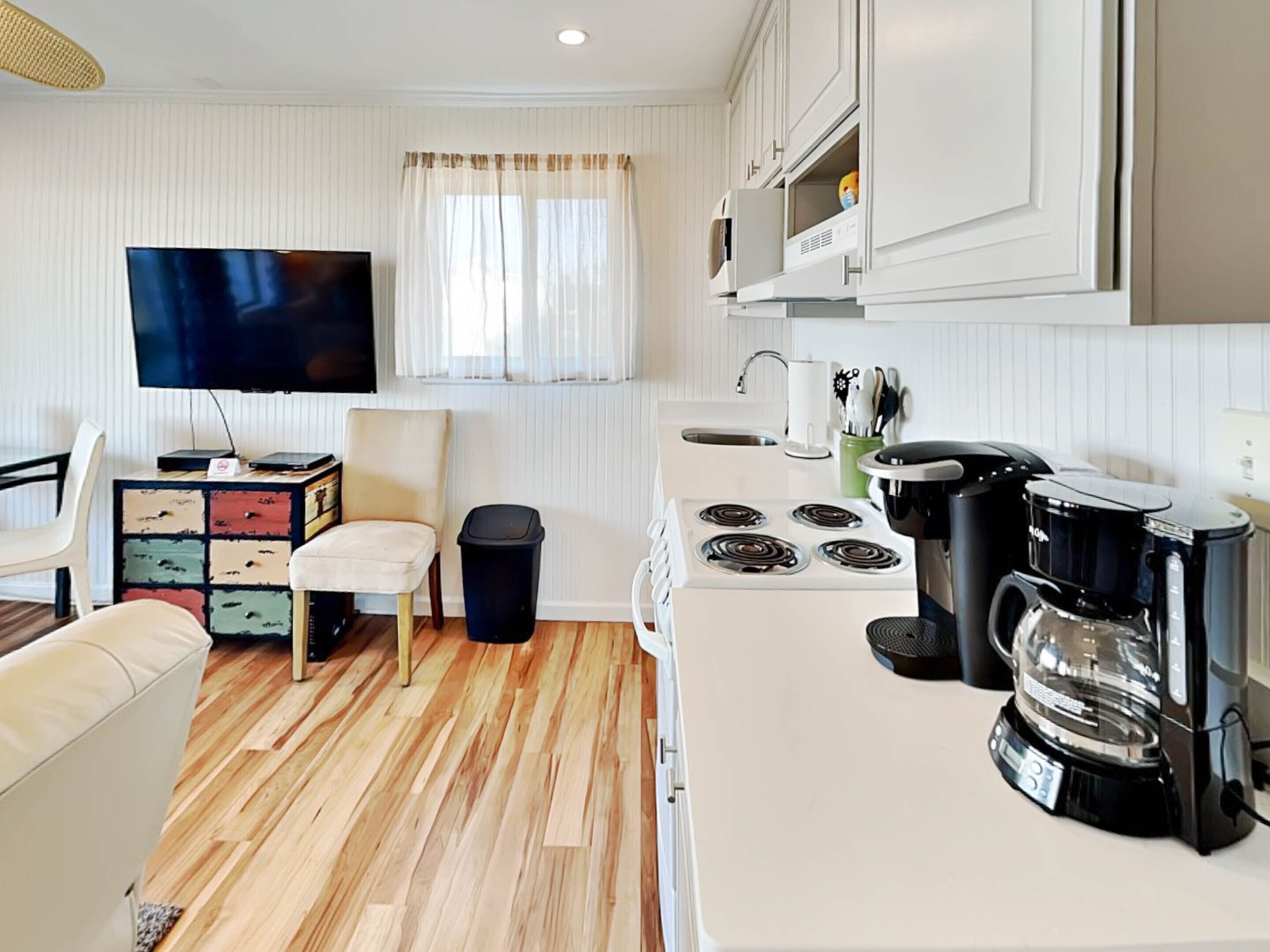 A compact kitchen with a stove, microwave, coffee maker, and a television.