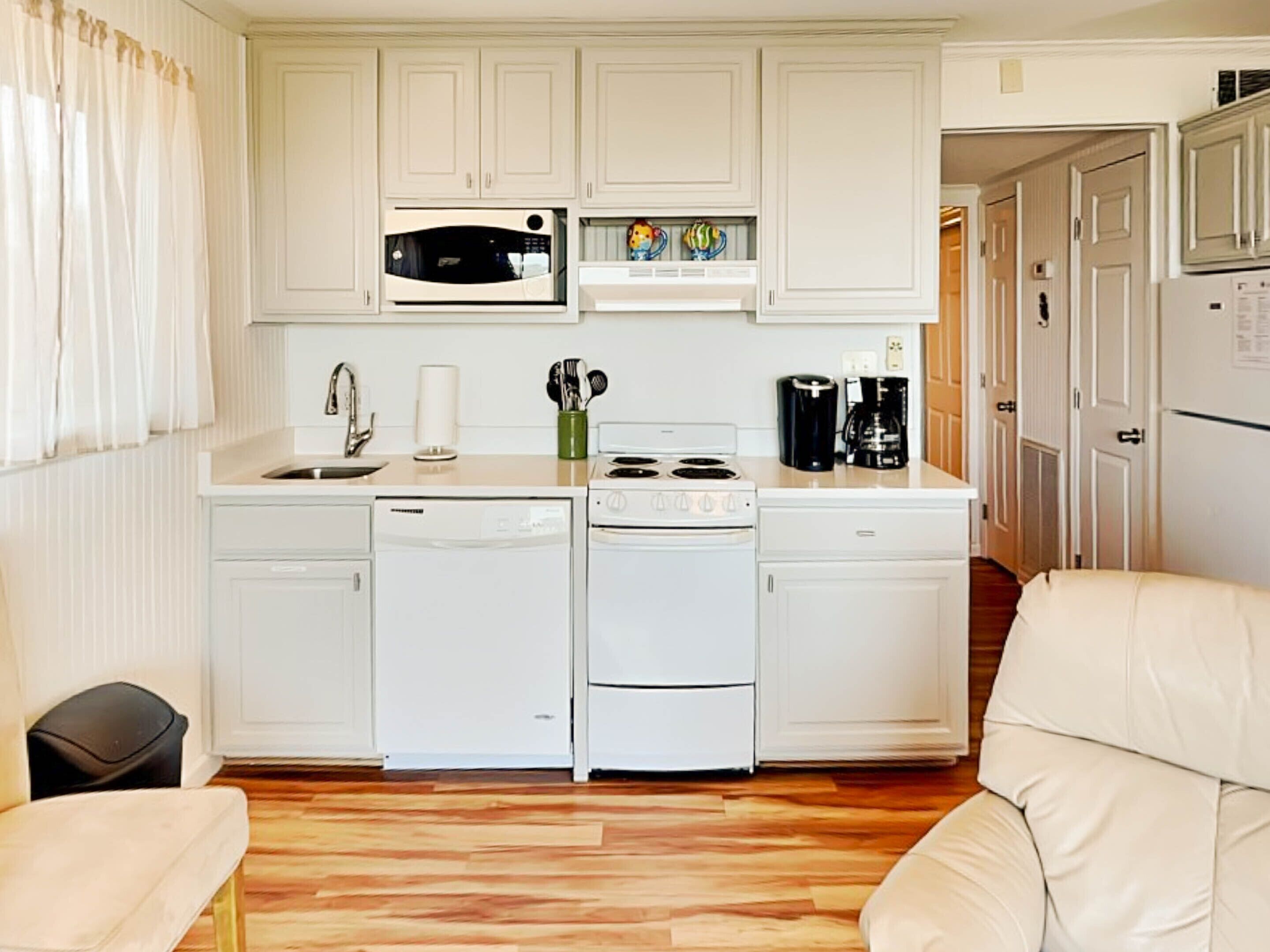 A compact kitchen with white cabinetry, a microwave, a coffee maker, and a dishwasher.