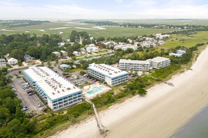 A coastal hotel with multiple buildings, a parking lot, and a beach.