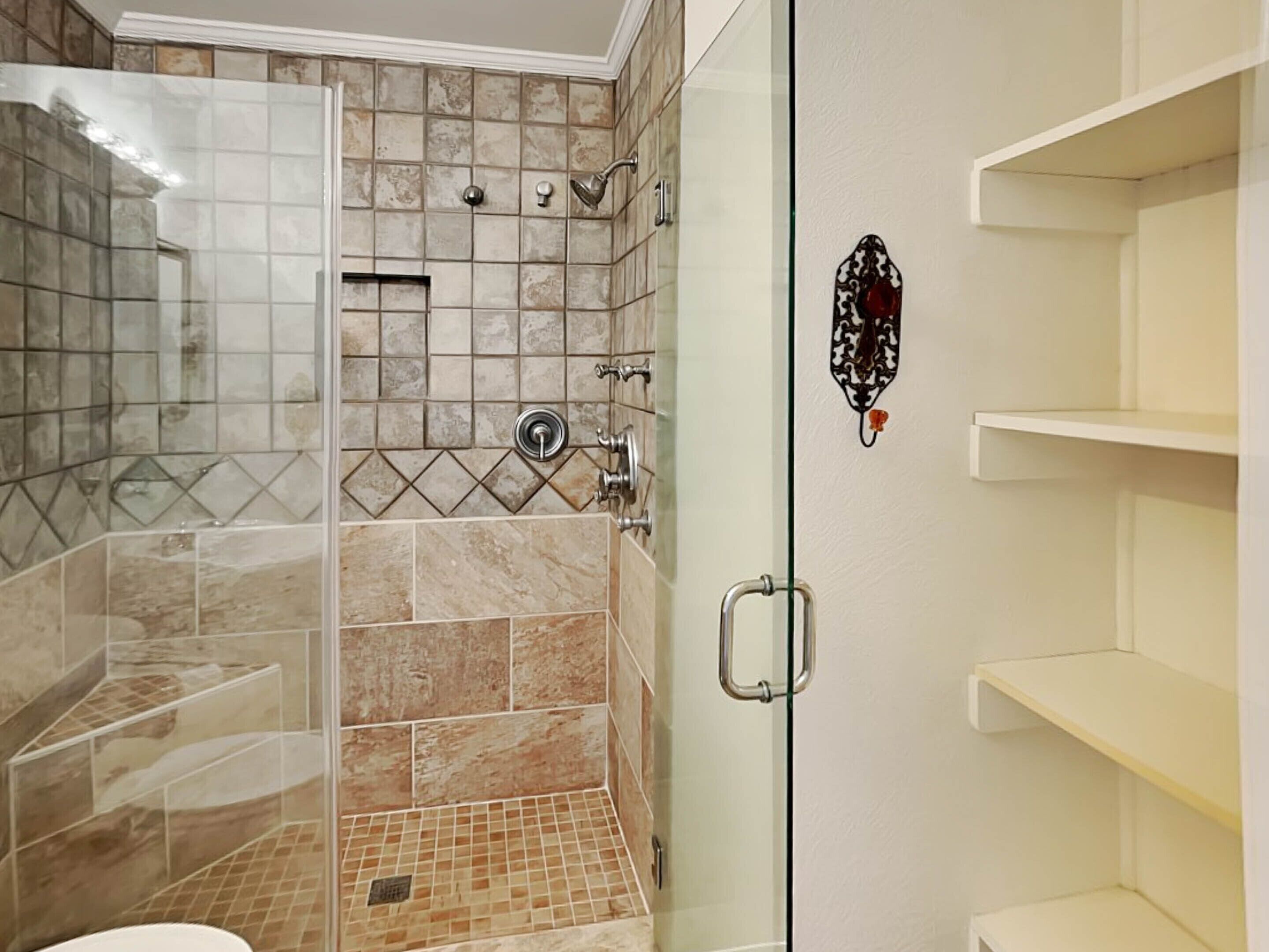 Un baño con cabina de ducha de vidrio, paredes de azulejos y un lavabo blanco.