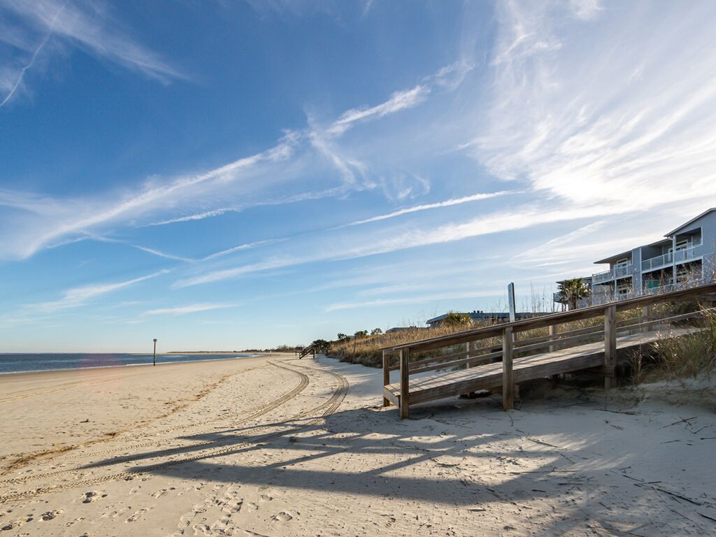 A beach with a wooden walkway leading to a building with balconies overlooking the ocean.