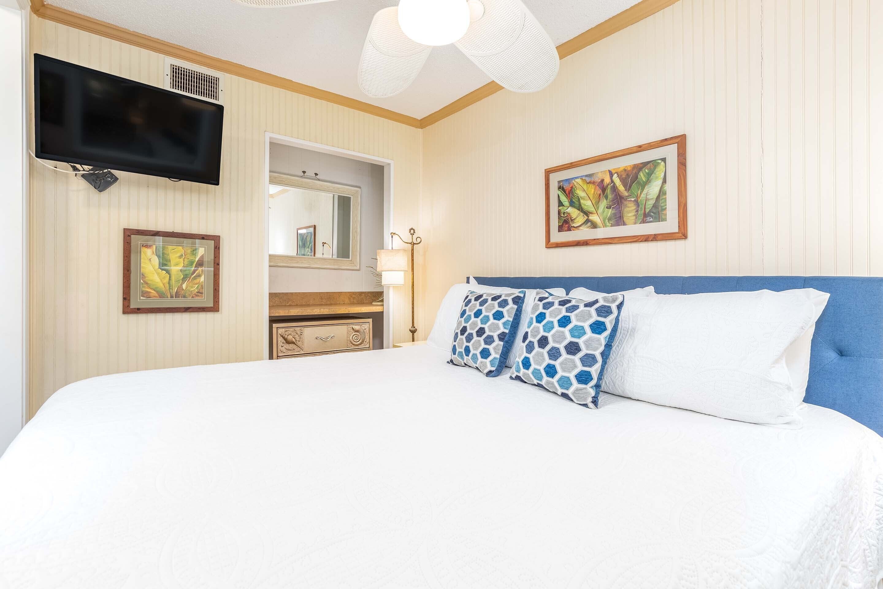 Une chambre d’hôtel avec un grand lit, un téléviseur à écran plat fixé au mur, une commode, un miroir et un tableau encadré au mur.
