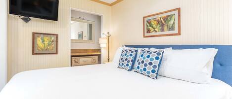 Une chambre d’hôtel avec un grand lit, un téléviseur à écran plat fixé au mur, une commode, un miroir et un tableau encadré au mur.