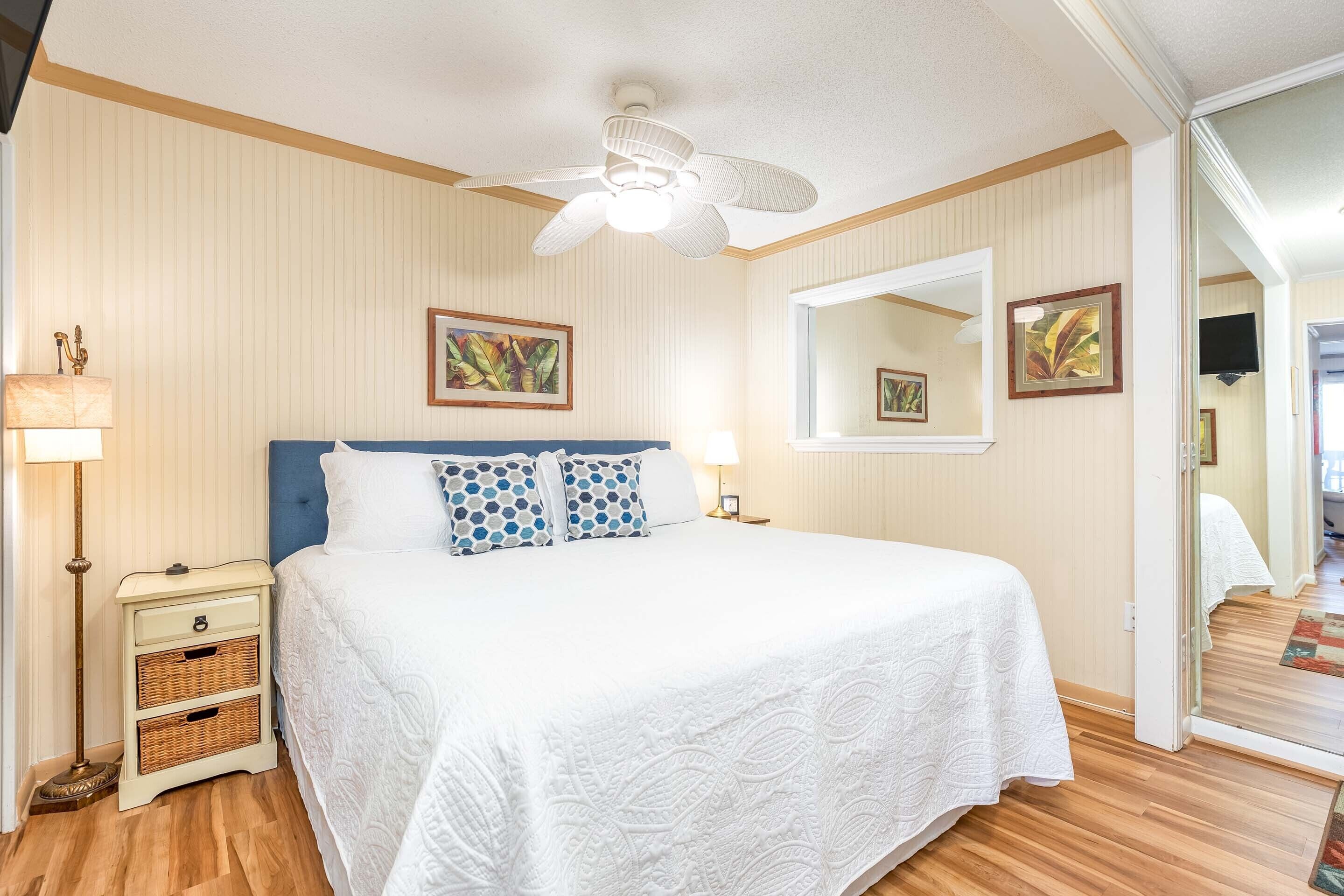 Un dormitorio con cama, mesita de noche, lámpara, ventilador de techo y espejo.