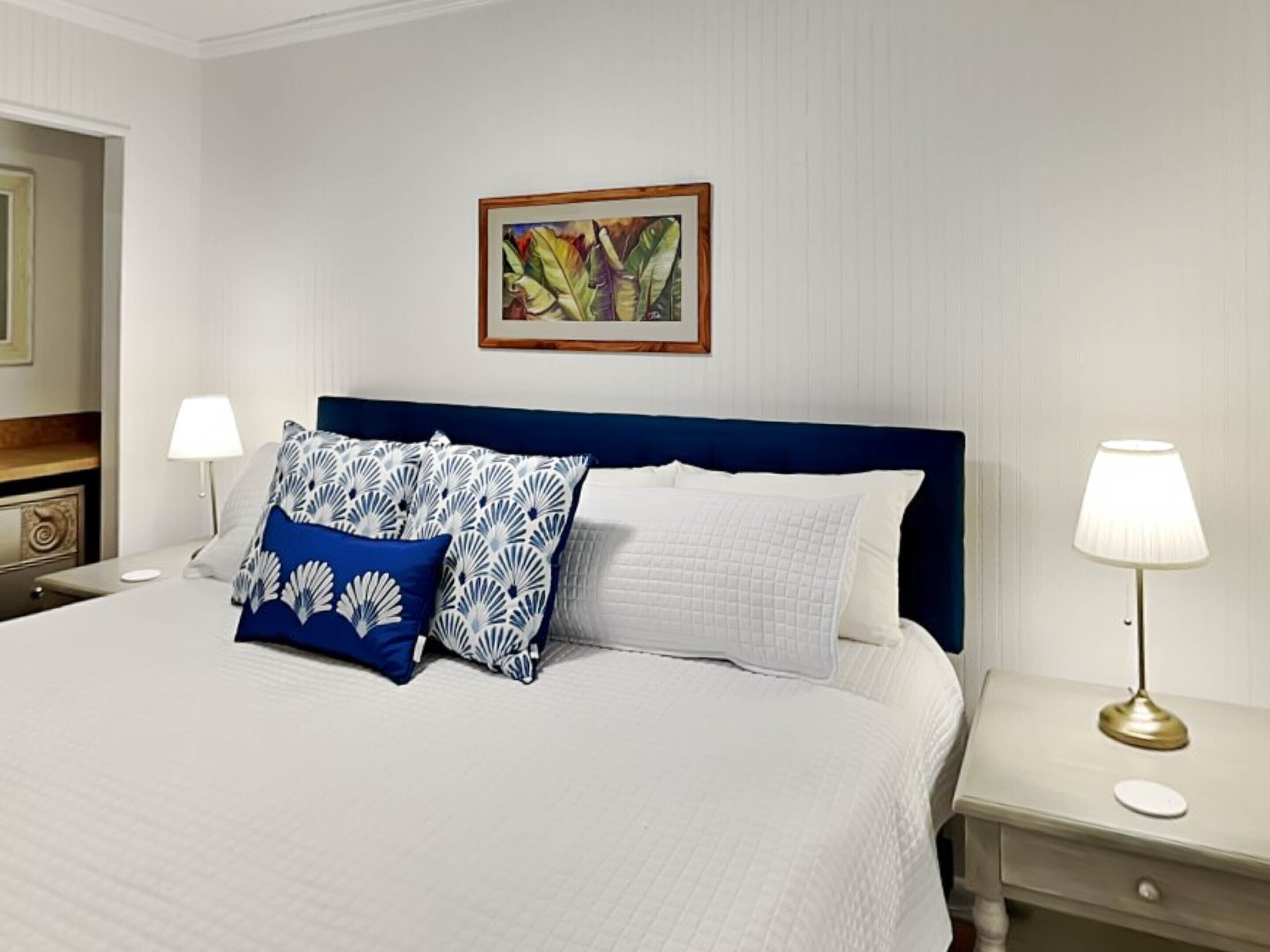A neatly made bed with white and blue patterned pillows, a blue headboard, and a framed artwork on the wall.