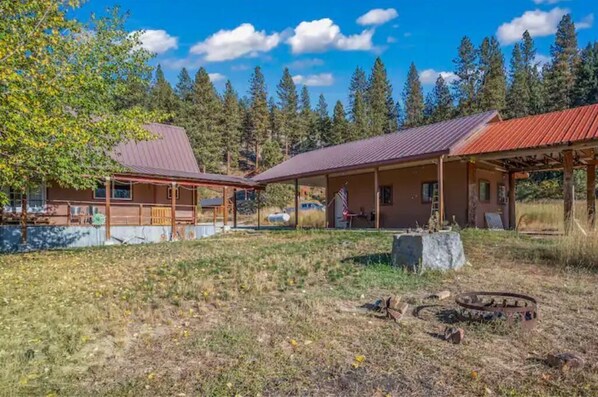 A rustic cabin with a metal roof, surrounded by a grassy area and trees.