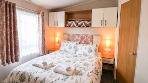 Un dormitorio con cama, dos mesitas de noche, un armario y una ventana con cortinas.