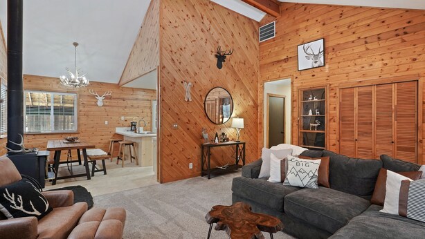 Een gezellig chaletinterieur met een eethoek, een woonkamer met een bank en een bijzettafeltje, houten wanden en een kroonluchter.