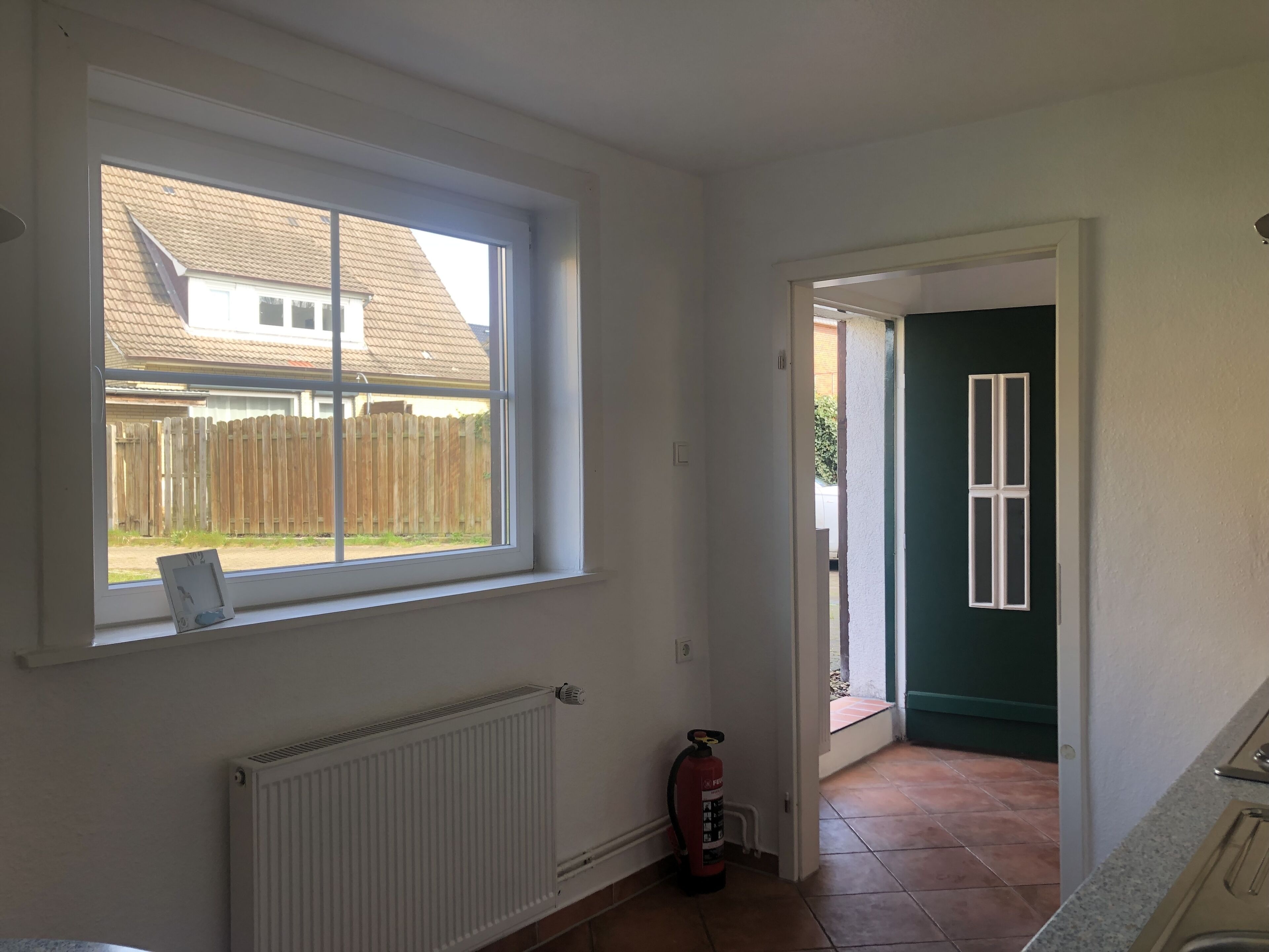 A room with a large window, a radiator, a fire extinguisher, and a door leading to an outdoor area.