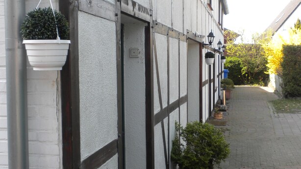 A narrow brick pathway leading to a building with white walls and dark wooden beams. There are hanging black lanterns and potted plants along the path. - Casa del mar - casa 1 (Cuxhaven)