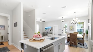A modern kitchen with a central island, stainless steel appliances, and a dining area with wicker chairs. - The Way Of Water 3 Bedroom Home by RedAwning (Panama City Beach)