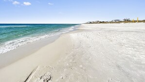 A beach with clear blue water, sandy shore, and houses in the background. - The Way Of Water 3 Bedroom Home by RedAwning (Panama City Beach)