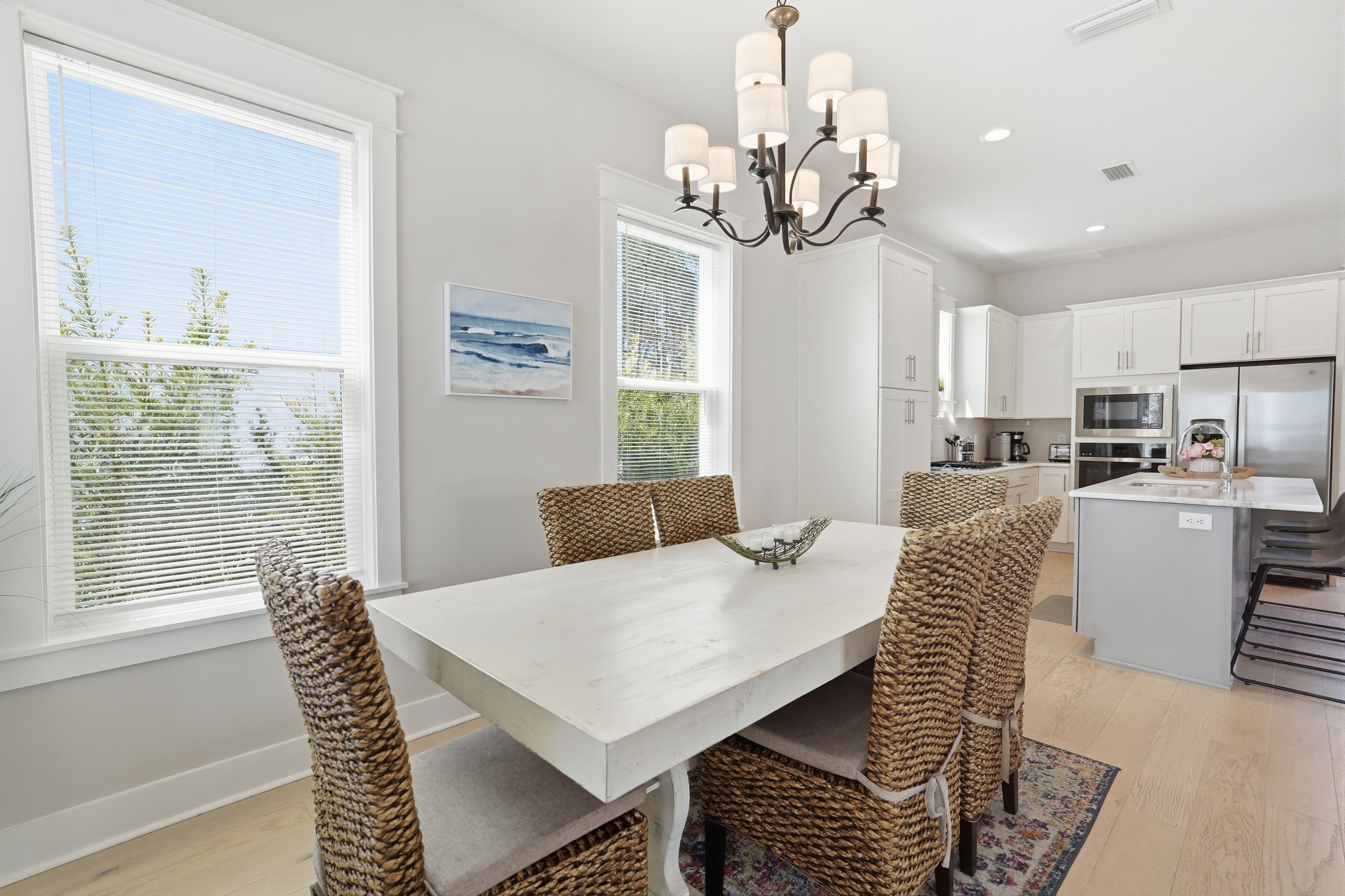 A modern kitchen with white cabinetry, a central island, and a dining area with wicker chairs.