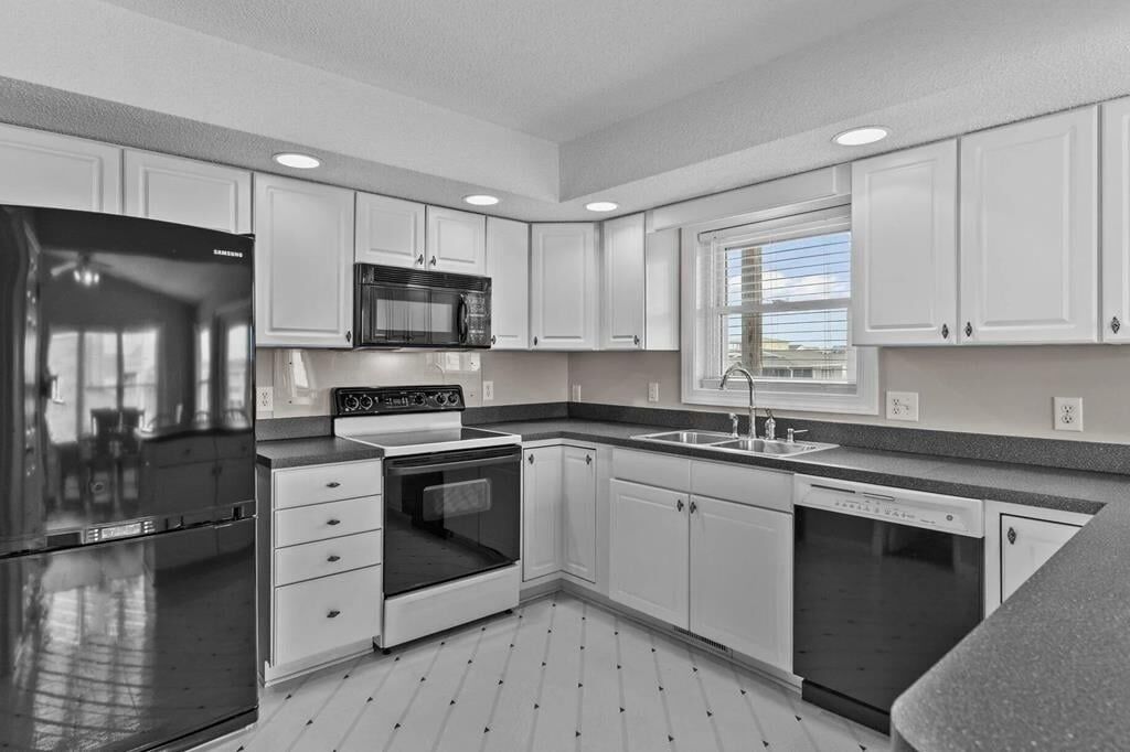 A modern kitchen with white cabinetry, a stainless steel refrigerator, a microwave, an oven, a dishwasher, and a window providing natural light.