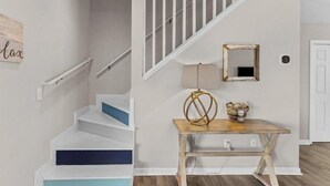 A staircase with white railings, a wooden console table with a lamp, and a wall-mounted mirror.