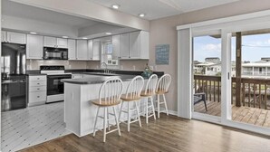 A modern kitchen with white cabinets, a central island with bar stools, and a large sliding glass door leading to a deck.