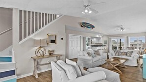 A spacious living area with a staircase, white sofas, a wooden coffee table, and a ceiling fan.